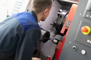 Factory worker is maintaining CNC metal lathe